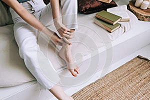 Woman sitting on the bed massages her foot, close-up. Woman with a slender body massages the leg, Young woman massaging her foot