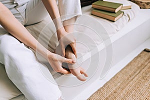 Woman sitting on the bed massages her foot, close-up. Woman with a slender body massages the leg, Young woman massaging her foot
