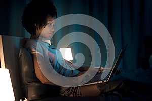 Woman sitting in bed at night and connecting with her laptop
