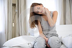 Woman sitting on the bed with pain in neck photo