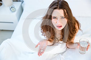 Woman sitting on bed with pills and glass of water
