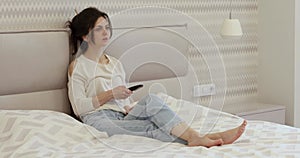 woman sitting on the bed and watching TV using remote control