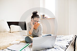 Woman sitting on bed, working on laptop, calling. Home office.