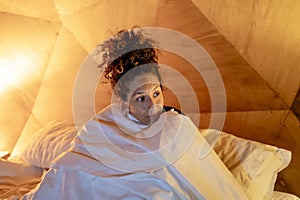 Woman sitting in bed wrapped in sheets.