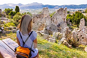 Woman sitting bench above ruins.