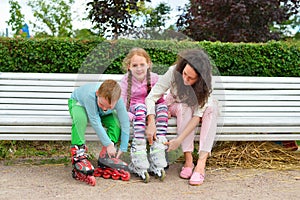 A woman sitting on a bench and helps her children to fasten the