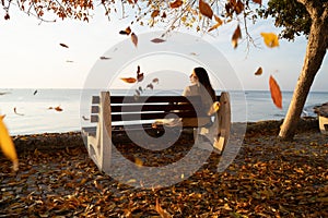 Woman sitting on a bench while leaves are falling