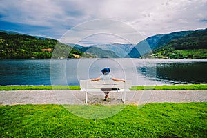 Woman sitting on a bench looking at the fjord in Ulvik, Norway. Fjord coastal promenade in Ulvik, Hordaland county, Norge. Lonely