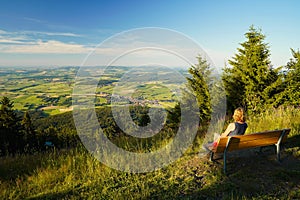 A woman sitting on a bench, looking from mount Hohenbogen to Neukirchen Heiligblut, a small town in the Bavarian Forest