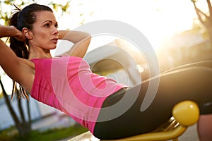 Woman sitting on bench outside doing situps.