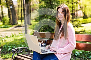 Woman sitting on bench in park talking using laptop.