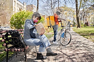 Woman sitting at the bench and peeking at the paper package at her order