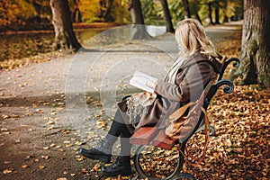 Woman sitting on bench and reading book in autumn park