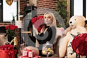 Woman sitting beside big bear gift holding red roses bouquet