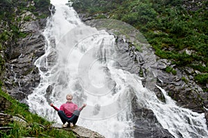 Woman sitting at the big powerful waterfall.