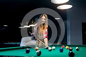 Woman sitting on billiard table and going hit ball