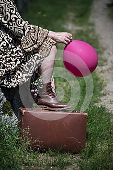 woman sitting in border the road forest with a suitcase and pik ballon