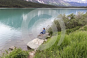 Woman sitting on a boulder next to a lake.