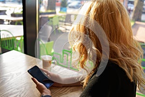 A woman is sitting in a cafe with a cup of cappuccino and is using a smartphone