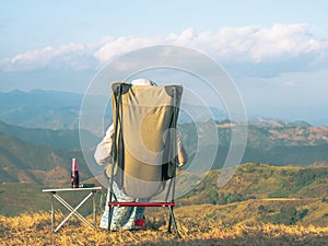 A woman sitting on camping chair facing to the mountain view.