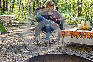 Woman sitting in camping chair with mug of coffee at campsite