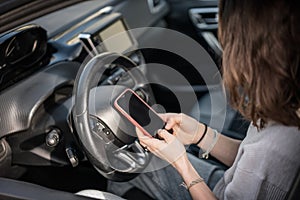 Woman sitting in a car in the driver& x27;s seat looking at a smartphone, paying for parking and navigating in the city
