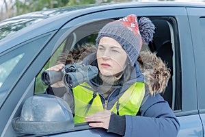 Woman sitting in car looking through binoculars