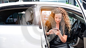 The woman sitting in the car and looking at her smart phone. Automobile Application. Auto Leasing Business. Digital Business.