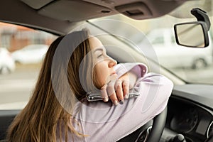 Woman sitting in car with phone in her hands. She has dreamy mood. Dark gloomy weather