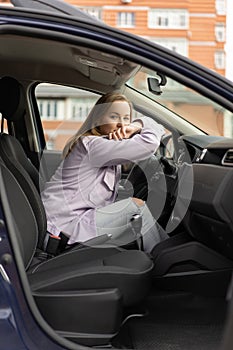 Woman sitting in car with phone in her hands. She has dreamy mood. Dark gloomy weather