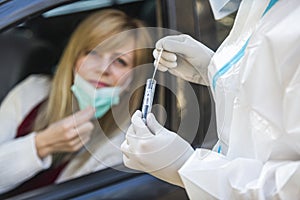 Woman sitting in car, waiting for medical worker in PPE to perform drive-thru COVID-19 test