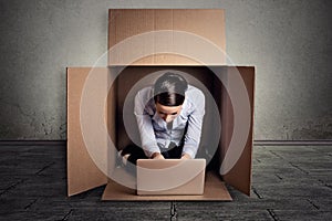 Woman sitting in carton box working on laptop computer