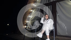 A woman is sitting in a chair on a balcony at night