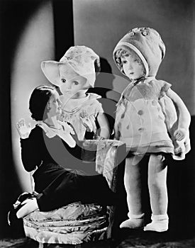 Woman sitting on a chair and looking at two oversized dolls