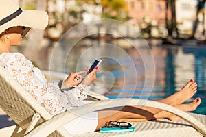 Woman sitting in chair by the swimming pool and using smartphone