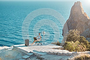 Woman sitting on chair and typing on laptop, seascape on background. Business travelling and distance work concept