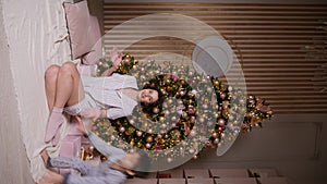 woman is sitting at a Christmas tree with a garland at home and a cheerful man and a boy jump on both sides. home