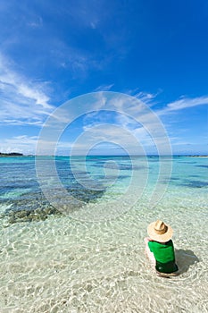 Woman sitting in clear shallow water of a tropical beach, Amami Oshima Island, Japan