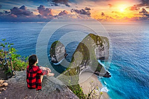 Woman sitting on cliff and looking at sunset at Kelingking Beach in Nusa penida island, Bali, Indonesia. photo