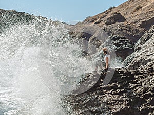 Woman sitting on cliff`s edge near sea with big splashes
