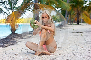 Woman sitting with coconut on the white sand beach