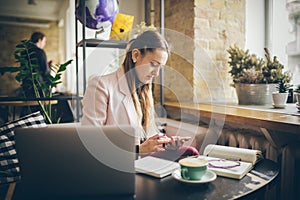 Woman sitting coffee shop wooden table, drinking coffee and using smartphone. Woman Using Phone In Cafe. Student learning online.