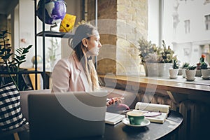 Woman sitting coffee shop wooden table, drinking coffee and using smartphone. Woman Using Phone In Cafe. Student learning online.