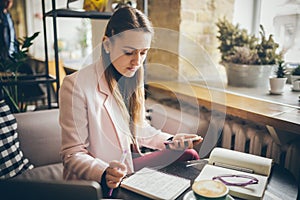 Woman sitting coffee shop wooden table, drinking coffee and using smartphone. Woman Using Phone In Cafe. Student learning online.