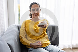 Woman sitting comfortable at home sofa watching tv pointing remote control for changing tv channel program