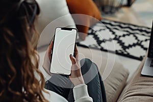 Woman sitting on couch, holding cell phone with white screen using thumb gesture