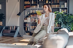 Woman sitting on couch in the morning, reading book at home