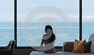 Woman sitting on couch, with ocean view in raining day