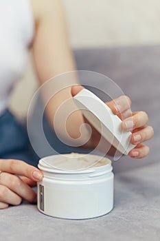 Woman sitting on couch opening jar of cosmetics cream