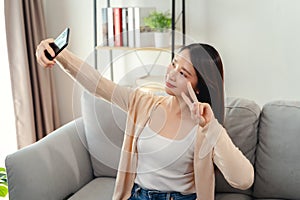 A woman is sitting on a couch and taking a selfie with her cell phone